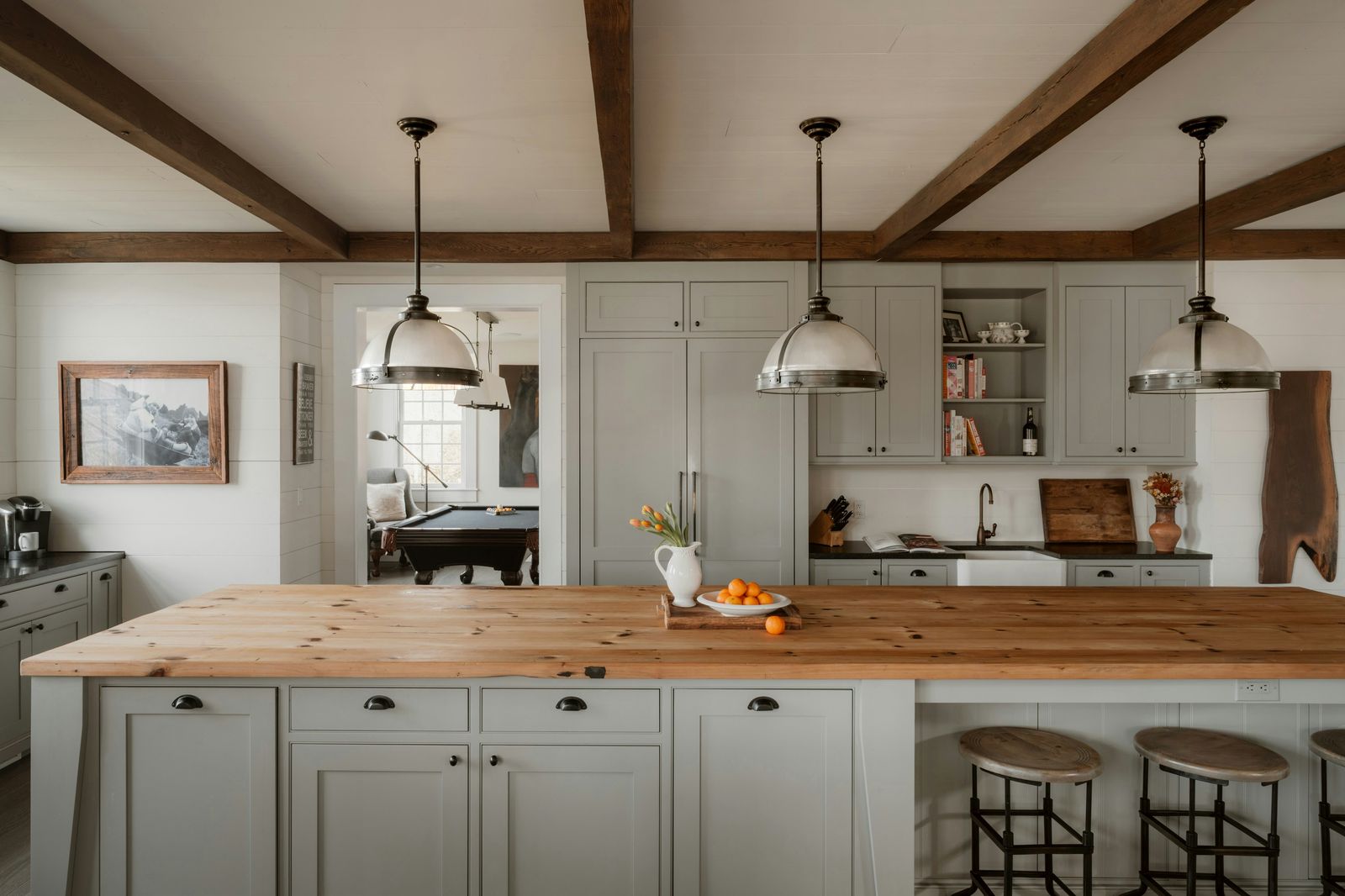 Kitchen with exposed beams, a live-edge wood island and sage cabinetry