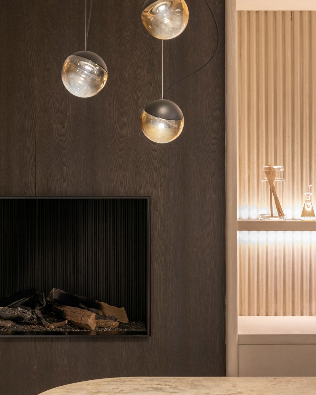 A dark oak fireplace wall with glass globe pendants and a travertine table