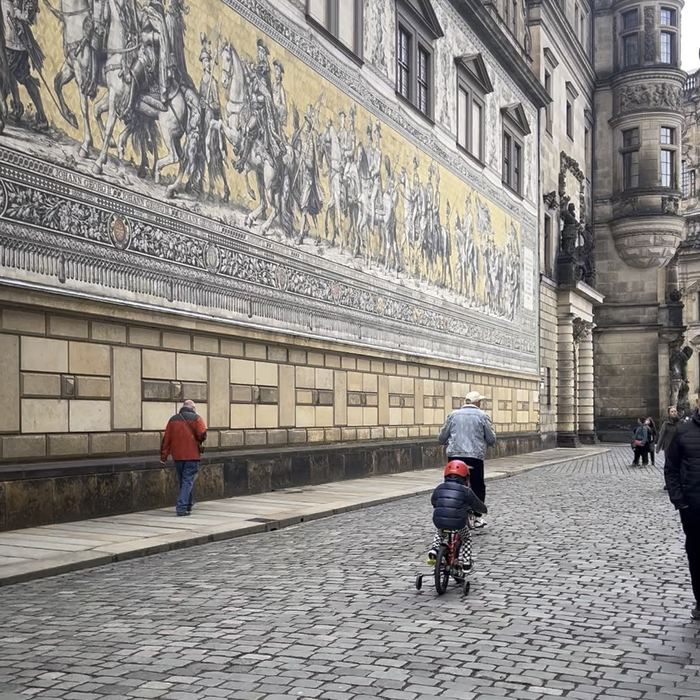 Their son cycling past the Fuerstenzug mural in Dresden